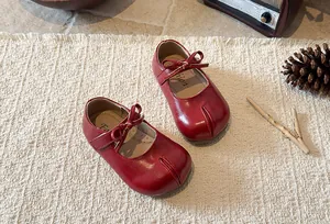 Close-up detail of red girl's Mary Jane princess shoes with elegant bow on a rustic mat