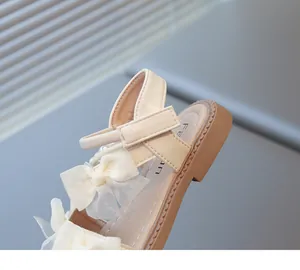 Detailed macro shot of the Velcro strap and delicate bow on a cream white girls' sandal.