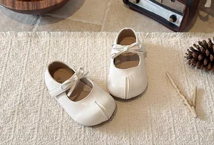 Close-up detail of white Mary Jane princess shoes with bow on a textured woven mat.