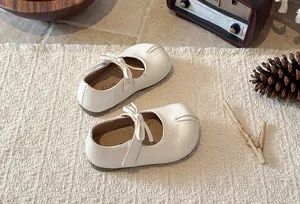 Top view of white vintage girls bow Mary Jane shoes on a textured cream rug background