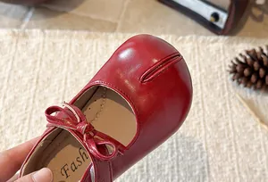 Close-up of red glossy girl's Mary Jane shoe featuring a bow and split-toe design
