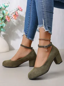 Detail van olijfgroene suède pumps met blokhak en elegant enkelbandje met bedeltje