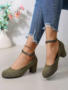 Detailweergave van olijfgroene suède pumps met blokhak en elegant enkelbandje en bedel aan de gesp