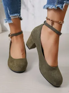 Detailweergave van olijfgroene suède-look pumps met blokhak en enkelbandje rond de enkel