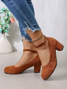 Zijaanzicht van bruine suède pumps met blokhak, enkelbandje en ronde neus