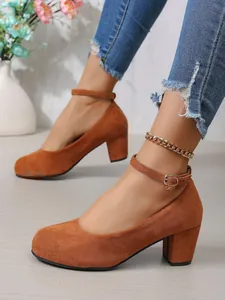 Detail van bruine suède pumps met blokhak, enkelbandje en een ronde neus
