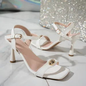 Elegant white high-heeled sandals featuring a gold ball detail and an ankle strap.