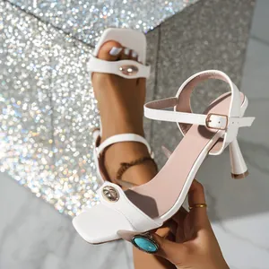Detailed view of elegant white soft leather high heel sandals with a gold metal buckle accent