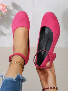 Gedetailleerde close-up van roze suède pumps met ronde neus en halvhoge blokhak.