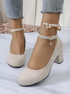 Detailweergave van beige suède pumps met blokhak en een elegante enkelband met bedeltje