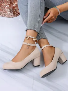 Close-up van beige suède pumps met blokhak, enkelbandje en kristallen hanger