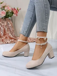 Detailweergave van beige suède pumps met ronde neus, blokhakken en een enkelbandsluiting.