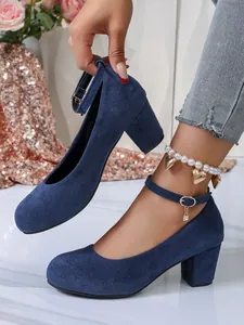 Gedetailleerd overzicht van marineblauwe suède pumps met blokhak en parel enkelbandje