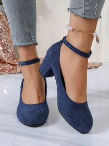 Detail van marineblauwe suède pumps met ronde neus, blokhakken en enkelbandjes.