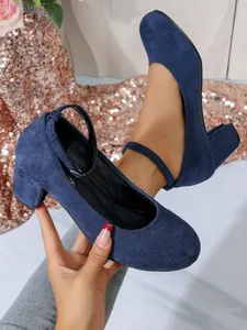 Gedetailleerd overzicht van marineblauwe suède pumps met blokhak en ronde neus design