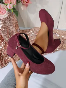 Detail van bordeauxrode suède pumps met blokhak, enkelbandje en een kristallen hanger.