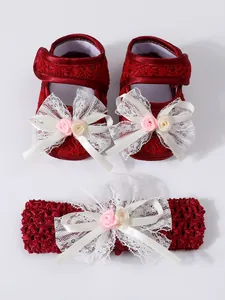 Detailansicht der roten Baby-Spitzenschuhe und des Stirnbands mit eleganten weißen Schleifen