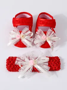 Detailansicht der roten Babyschuhe aus Spitze und des passenden Stirnbands mit weißen Schleifen