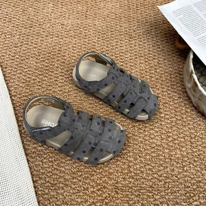 Detailansicht grauer Mädchen-Römersandalen mit lila Punkten auf braunem gewebtem Teppich