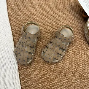 Detailansicht brauner Kindersandalen mit blauen Punkten auf einem braunen Webteppich