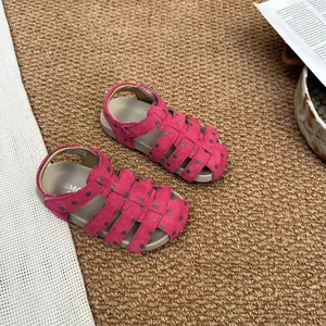 Detailansicht von rosa gepunkteten Gladiator-Sandalen für Mädchen auf einem Teppich.