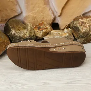 Dettaglio laterale di sandalo con zeppa beige con borchie metalliche e cuciture bianche a contrasto