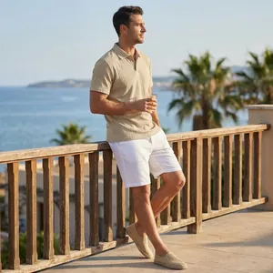 Vue en pied d'un homme portant un polo en maille jacquard beige sur un balcon au bord de la mer.