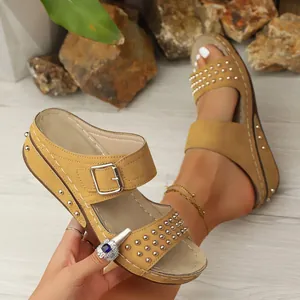 Primo piano di eleganti sandali con zeppa marroni con borchie metalliche e fibbia.
