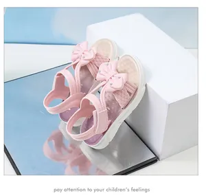 Detalle de sandalias rosas para niñas con lazo y pedrería sobre superficie espejo