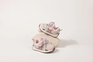 Due scarpe primi passi in rete traspirante rosa e verde su un supporto minimalista.