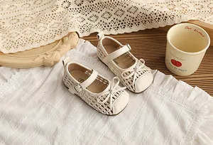 Detalle de sandalias trenzadas crema para niña con lazo y correa con hebilla.