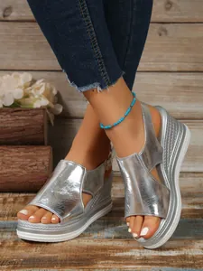Detail of stylish silver metallic wedge sandals featuring hollow-out design and peep toe.