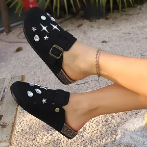 Close-up of black closed-toe clogs with sparkling star and gem decorations on a model.
