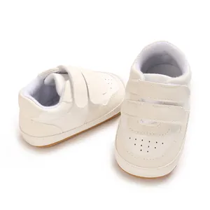 Detailed view of white infant walking shoes with dual velcro straps and rubber soles