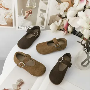 Scarpe Mary Jane in camoscio marrone per bambini con fibbie argentate su un tavolo.