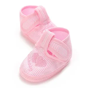 Gros plan de chaussures souples pour bébé à rayures roses avec broderie cœur et scratch.