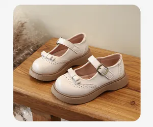 Scarpe Mary Jane color crema per bambina con fiocco e motivi brogue su panca di legno