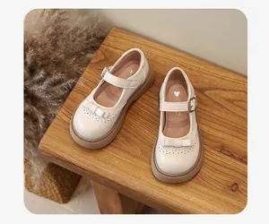 Eleganti scarpe Mary Jane beige per bambine con fiocco su una superficie di legno.