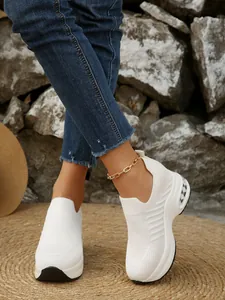 Weiße Fly-Knit Slipper mit dicker Plateausohle in einer Outdoor-Umgebung.
