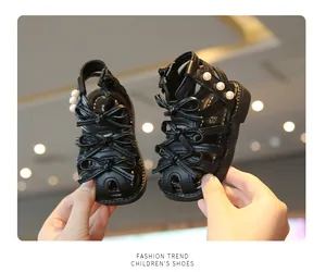 Nahaufnahme von schwarzen Baby-Römersandalen mit dekorativen Schleifen und Perlendetails.