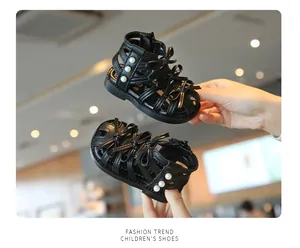 Nahaufnahme von schwarzen Römersandalen für Mädchen mit Perlen- und Schleifendetails.