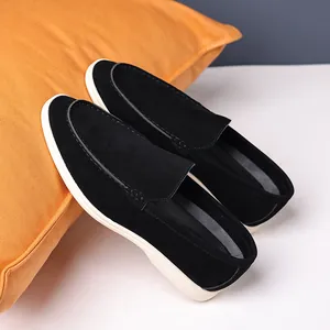 Pair of premium black suede loafers with white soles resting on an orange pillow prop