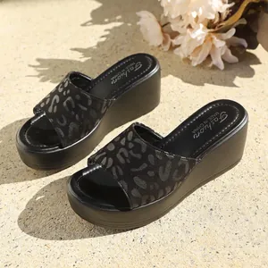 Primer plano de sandalias con cuña negras con tira de ante con estampado de leopardo.