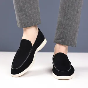 Close-up of black suede loafers worn with grey pinstripe trousers in a studio setting.