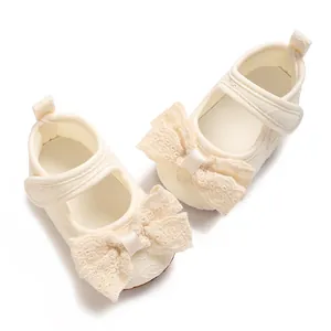 Close-up of cream baby princess shoes with delicate lace bow and floral texture.