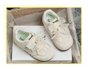 Detail of beige children's sneakers featuring pearl bow and delicate lace ribbon