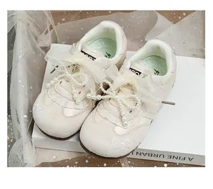 Detailed view of girls' beige sneakers with decorative pearls, lace, and organza bows.