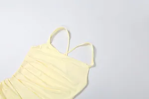 Detail view of a light yellow ruched dress featuring thin spaghetti straps and pleats.