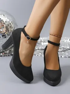 Detail of black suede chunky heel pumps with ankle strap and heart charm.