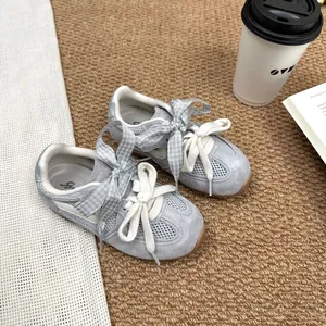 Detailed top view of grey mesh girls' sneakers with decorative plaid ribbons on a rug